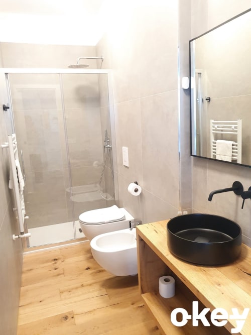 Bagno moderno con lavabo nero, wc bianco, doccia con box in vetro, mobile in legno e piastrelle beige a Bari