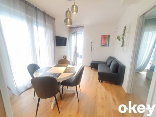 Moderna sala da pranzo in appartamento fronte mare a Bari con pavimento in legno, tavolo da pranzo, sedie nere, divano, TV e illuminazione con lampade a sospensione