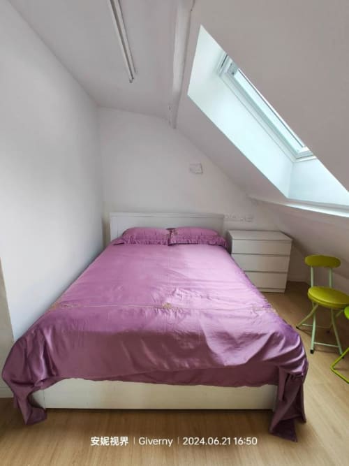 Chambre mansardée au Coin des Artistes avec literie rose, lucarne, parquet et fauteuil vert