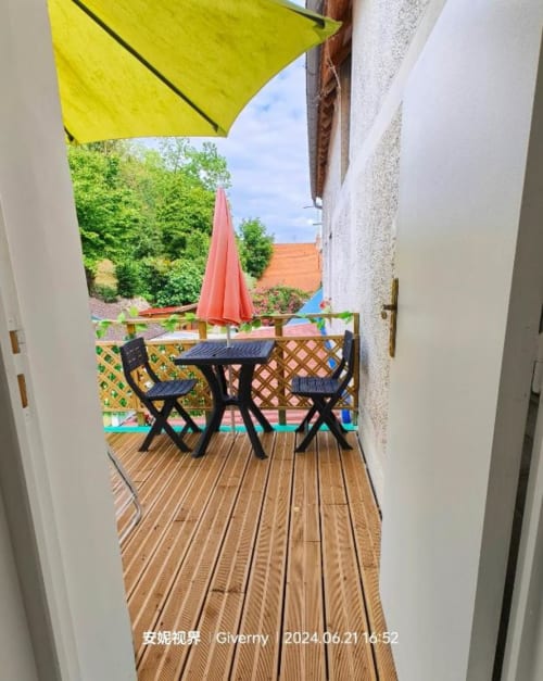 Terrasse extérieure du B&B Le Coin des Artistes avec table noire, chaises, parasol jaune et rouge surplombant le jardin