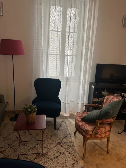 Salon de la Conciergerie Maurin à Arles avec fauteuil noir, mobilier vintage, lampadaire et rideaux voilages.