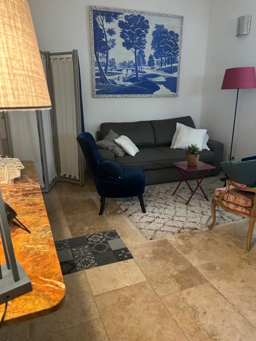 Salon moderne à la Conciergerie Maurin à Arles avec canapé noir, fauteuil bleu et tableau paysage bleu