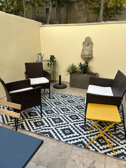 Coin détente cosy à la Conciergerie Maurin à Arles avec fauteuils en rotin, tabouret jaune et tapis géométrique