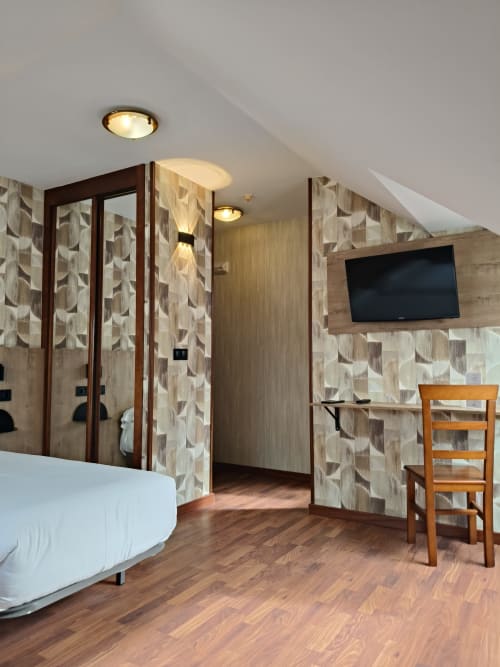 Habitación moderna del Hotel Puerto de Candás con camas individuales, papel tapiz geométrico, TV de pared, suelo de madera y techo inclinado