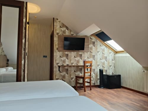 Habitación doble con camas gemelas en hotel Candás, empapelado geométrico, televisor, muebles de madera y tragaluz