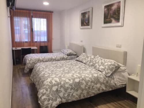 Double bedroom with extra bed at Hotel Skyline Alcorcón, featuring patterned bedding, windows with curtains, and framed