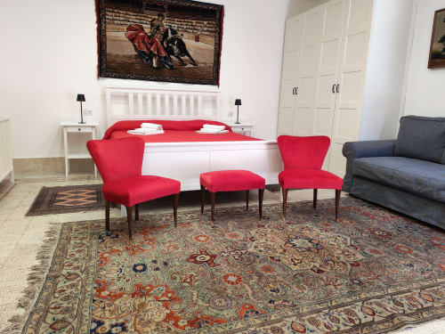 Camera da letto di Sicily Confort Maison con sedie rosse, letto bianco, tappeto ornamentale e opere di tauromachia