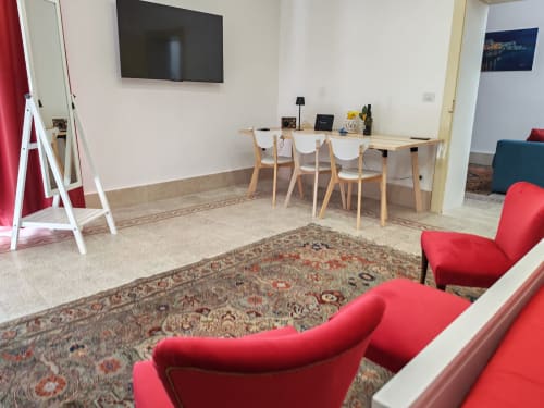 Soggiorno moderno con poltrone rosse, tavolo in legno, TV a muro e tappeto decorativo - Sicily Confort