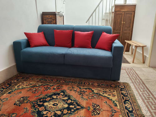 Divano blu con cuscini rossi nel salotto dell'appartamento Sicily Confort Maison, arredato con tappeti decorativi