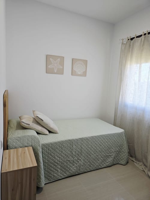 Dormitorio luminoso en Ona vacaciones Apartamento Miramar en Gandía con cama acolchada, mesita de noche de madera y decoración de tema costero