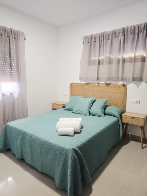 Dormitorio luminoso en Ona vacaciones en Gandía con ropa de cama turquesa, cabecero de ratán y cortinas semitransparentes