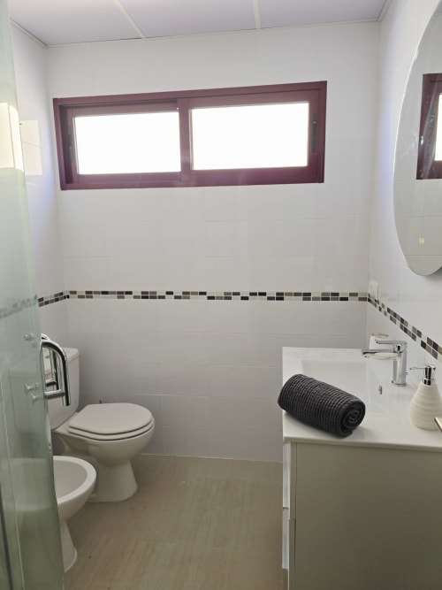 Baño moderno en Apartamento Miramar, Ona vacaciones, Gandía con azulejos blancos, detalles oscuros, inodoro, lavabo y ventana