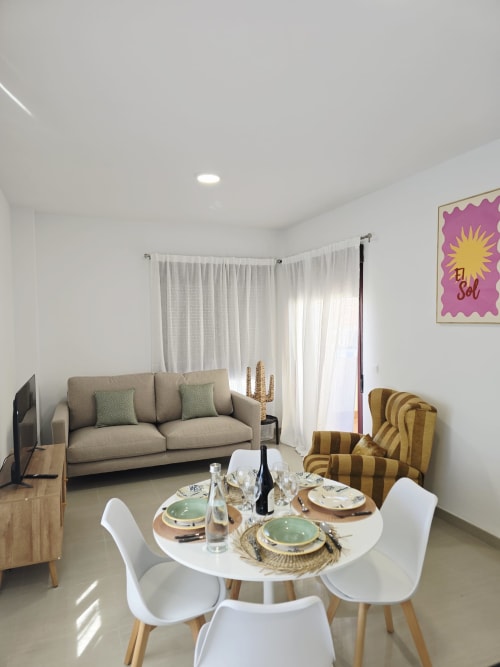 Zona de estar abierta y moderna en Ona vacaciones, Gandía con mesa de comedor, sofá beis y butaca a rayas