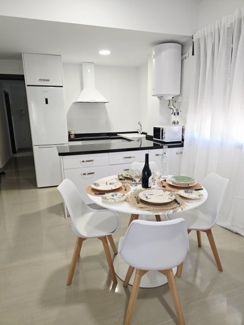 Cocina-comedor moderno en Ona Vacaciones Apartamento Miramar en Gandía con electrodomésticos blancos y mesa redonda preparada