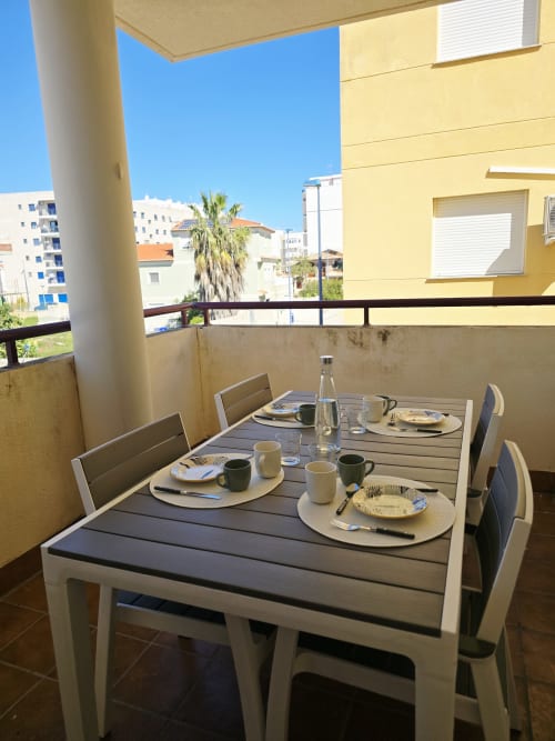 Zona de comedor en el balcón de Ona Vacaciones Gandía con mesa preparada con vistas a palmeras y edificios costeros