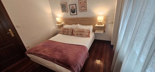 Dormitorio moderno en hotel Bizkar Bare, Vizcaya, con cama queen, manta burdeos, cabecero de madera e iluminación ambiental