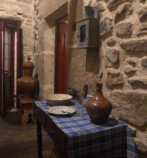 Historic stone kitchen with traditional pottery, table setting, and red doors at Quinta das Pias, Portugal