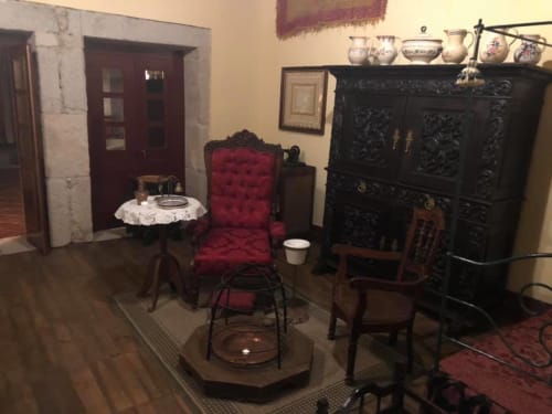 Historic Portuguese bedroom with burgundy upholstered chair, ornate black cabinet, and period furnishings at Quinta das Pias