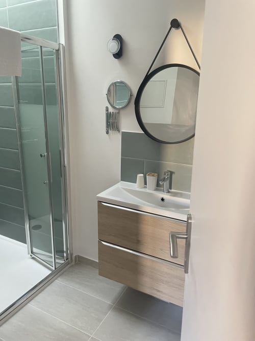 Salle de bain moderne avec douche ouverte, meuble vasque en bois et miroir rond à l'Hôtel Les Paquebots à Port-Vendres
