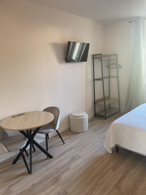 Chambre d'hôtel moderne aux Paquebots avec table ronde, chaise, téléviseur, étagères métalliques et lit à Port-Vendres