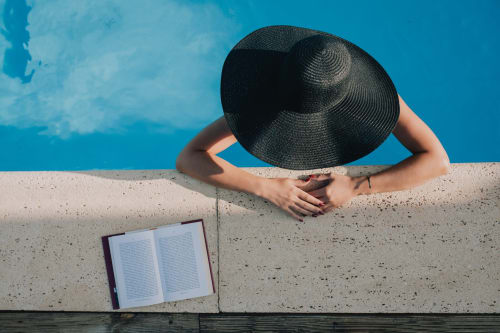 Pessoa com chapéu preto relaxando à beira da piscina na Herdade da Cova da Onça, Canha Portugal, com livro