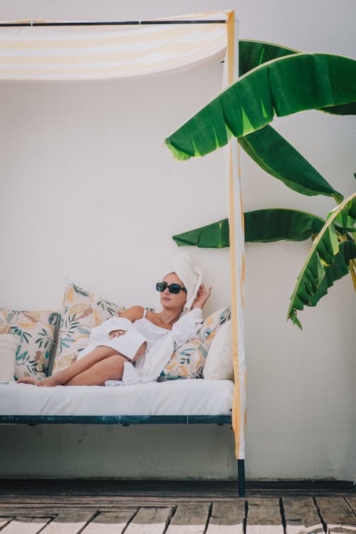 Mulher relaxando em cama com dossel e folhas tropicais de bananeira no hotel boutique Herdade da Cova da Onça em Canha, Portugal