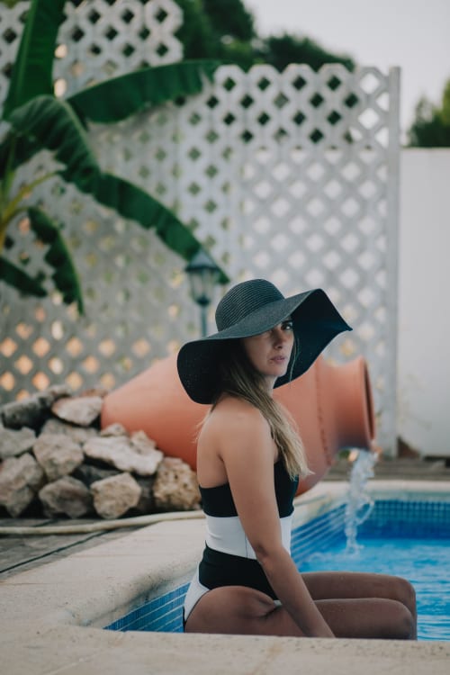 Mulher de chapéu preto abas largas à beira da piscina da boutique hotel Herdade da Cova da Onça em Canha, Portugal