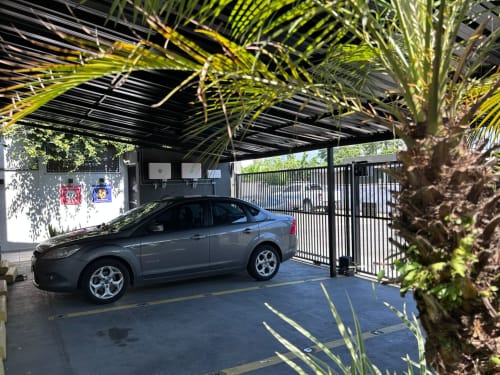 Sedan azul estacionado em garagem coberta com palmeiras e portão de ferro preto no apartamento BORA BORA HOSPEDAGENS em Joinville