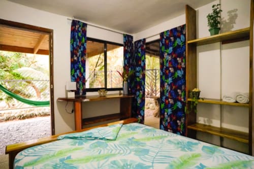Dormitorio colorido en Hotel Swell Pavones con ropa de cama de hojas tropicales, escritorio de madera y cortinas vibrantes con vistas a Pavones