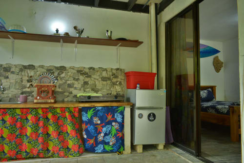 Acogedora habitación en Hotel Swell Pavones con kitchenette, detalles de telas coloridas, decoración vintage y cama visible a través de puerta de vidrio