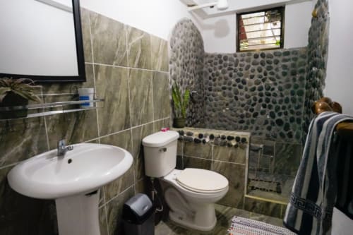 Baño moderno del Hotel Swell Pavones con lavabo redondo, inodoro y ducha con pared de guijarros