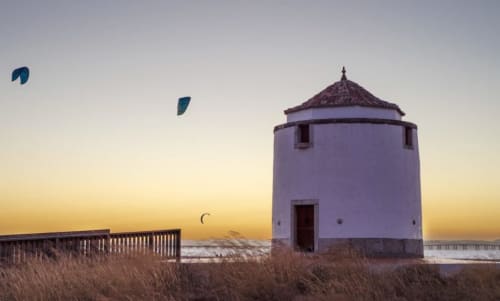 White windmill at Herdade da Cova da Onça at sunset with kites flying over Canha beach