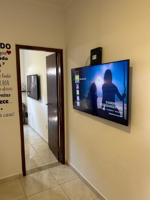 Sala de estar com TV de 50 polegadas exibindo Netflix, porta de entrada em madeira e paredes amarelas no apartamento BORA BORA HOSPEDAGENS