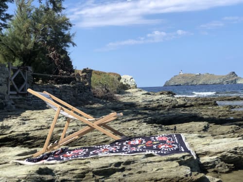 Chaise longue en bois et serviette colorée sur la plage rocheuse corse de la villa La Conciergerie du Cap Corse avec vue mer
