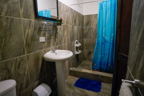 Baño moderno en la Habitación 2 del Hotel Swell Pavones con lavamanos pedestal, inodoro y cortina de ducha azul en Pavones, Costa Rica.