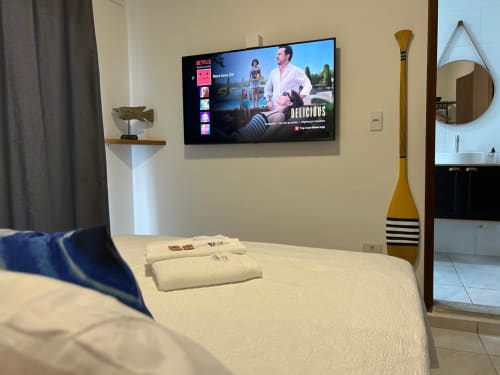 Quarto moderno em BORA BORA HOSPEDAGENS em Joinville com TV de 50 polegadas exibindo Netflix, roupa de cama branca, decoração em madeira
