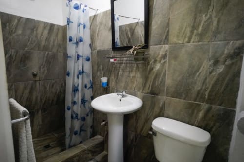 Baño moderno en la Habitación 3 del Hotel Swell Pavones, Pavones CR con azulejos grises, lavamanos de pedestal, inodoro y ducha azul