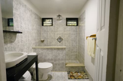 Baño moderno del Hotel Swell Pavones con ducha abierta, lavamanos redondo y detalles en piedra
