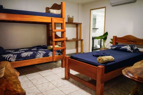 Habitación luminosa en Hotel Swell Pavones con litera de madera, cama individual con ropa de cama azul marino, piso de azulejos, aire acondicionado y espejo.