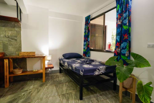 Habitación 6 del Hotel Swell Pavones con cama individual, muebles de madera, cortinas vibrantes y planta en maceta en Pavones, CR