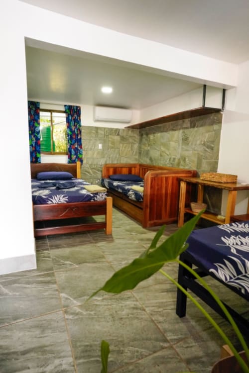 Hotel Swell Pavones Habitación 6: Dormitorio espacioso con camas de madera, ropa de cama azul marino, plantas verdes y piso de baldosas
