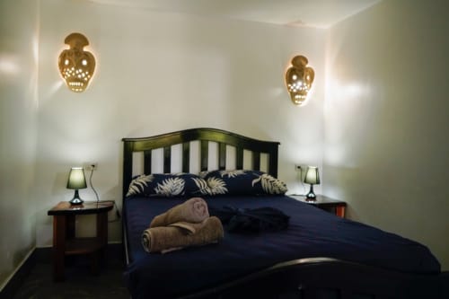 Habitación 6 del Hotel Swell Pavones con cama negra, ropa de cama azul marino, apliques de calavera dorados y mesitas de noche de madera con lámparas