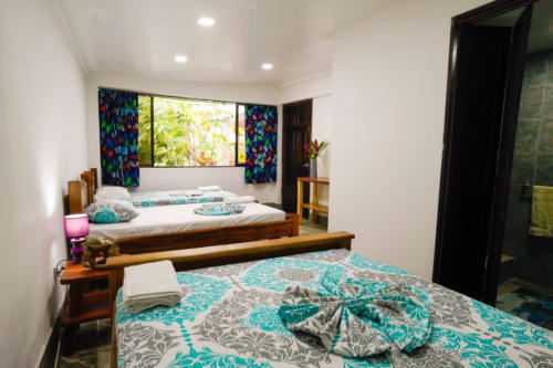 Habitación 7 del Hotel Swell Pavones con camas de madera, ropa de cama con patrón turquesa y cortinas coloridas con vistas tropicales