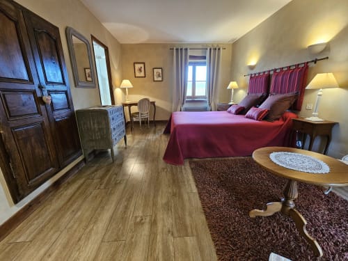 Suite élégante du Château de Ribourdin avec lit bordeaux, mobilier en bois et vue sur le jardin