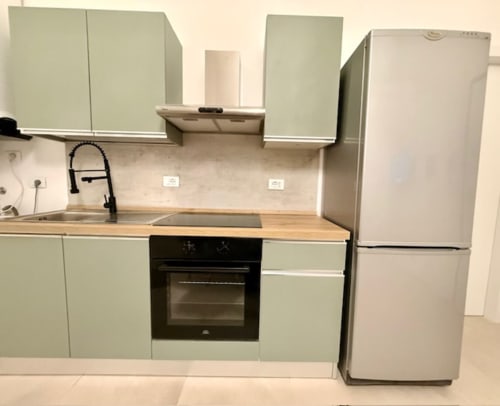Cucina moderna in appartamento Effi House Bologna con mobili verde salvia, piano in legno, forno nero e acciaio inossidabile