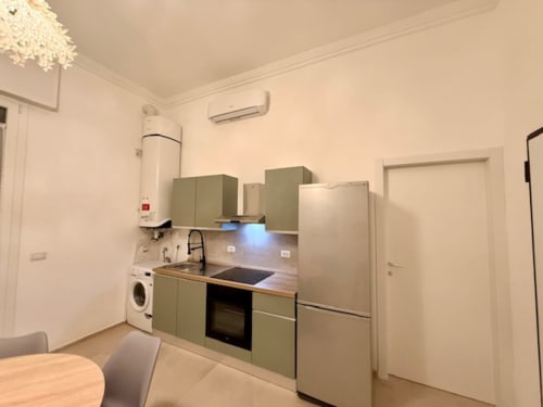 Cucina moderna nell'appartamento Effi House Bologna con mobili verde salvia, elettrodomestici in acciaio inox e piani di lavoro in legno