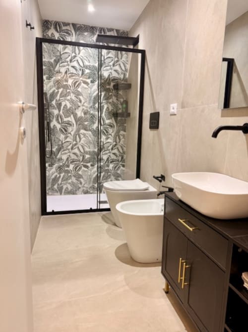 Moderno bagno nell'appartamento bolognese con doccia dai vetri neri, lavabo in ceramica bianca, wc e pavimento in piastrelle beige