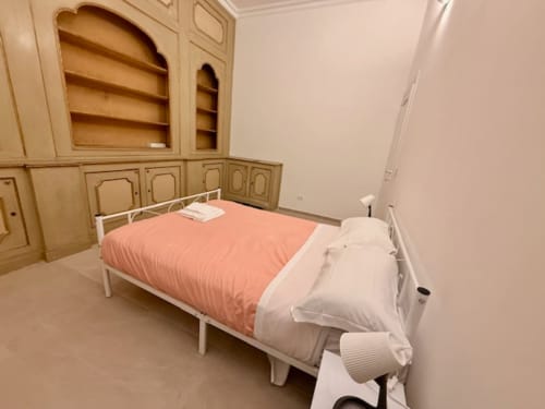 Camera da letto con letto in metallo bianco, biancheria coral pink, cuscini bianchi e armadio in legno con ripiani presso Effi House