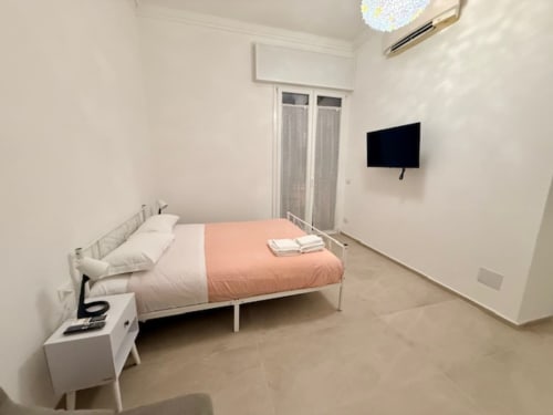 Camera moderna di Effi House Bologna con letto in metallo bianco, biancheria color corallo, TV a schermo piatto e arredamento minimalista