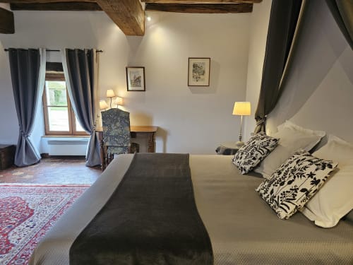 Chambre élégante du Château de Ribourdin avec poutres apparentes, coussins à motifs, bureau et vue sur les monuments de Chevannes